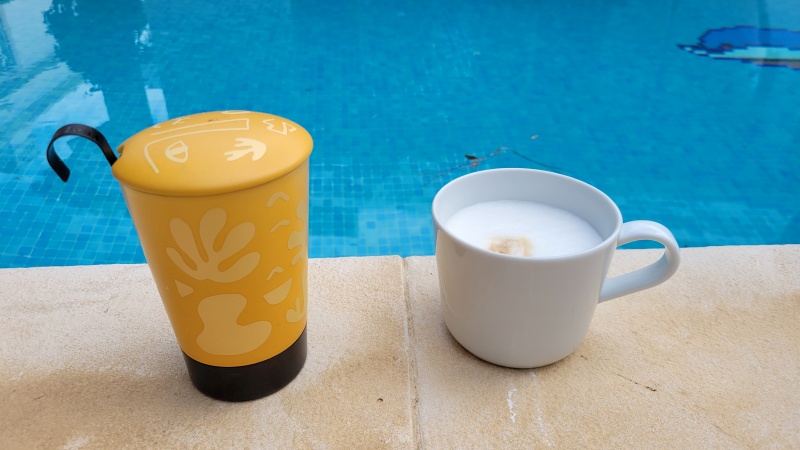 Tassen mit Tee und Kaffee am Beckenrand eines Pools.