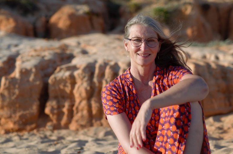 Frau in buntem Sommerkleid vor den Felsen der Algarve
