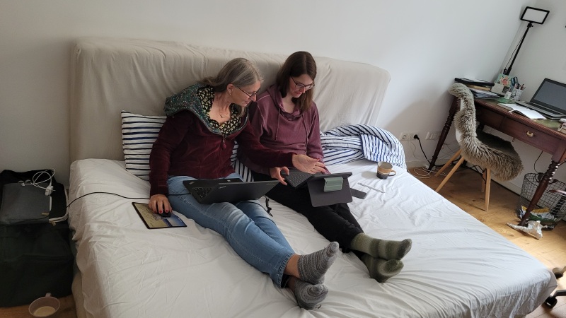 Zwei Frauen arbeiten sitzend auf einer Matratze an ihren Laptops.
